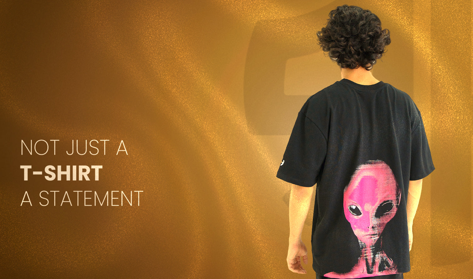 Person wearing a black t-shirt with an alien design on the back, standing against a brown background.